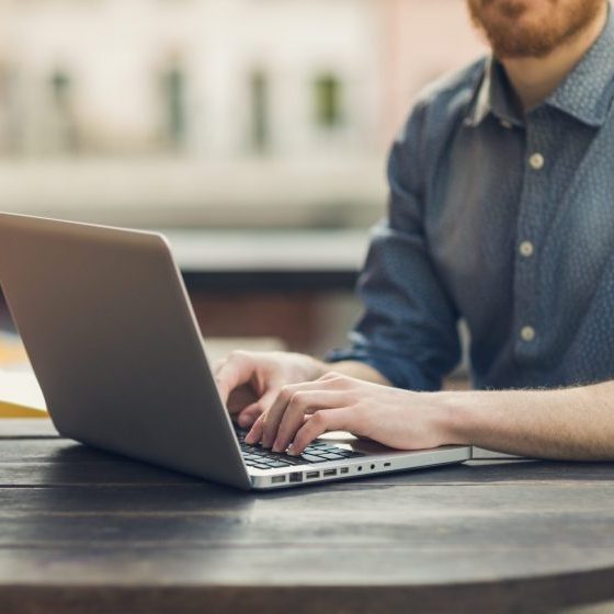 Unrecognizable man using a modern portable computer on an outdoor table, street on background